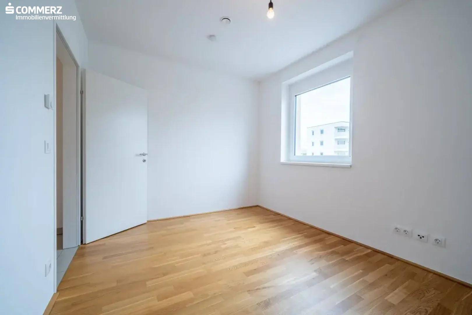 Helles Schlafzimmer mit Holzboden und großem Fenster, bereit für individuelle Einrichtung.