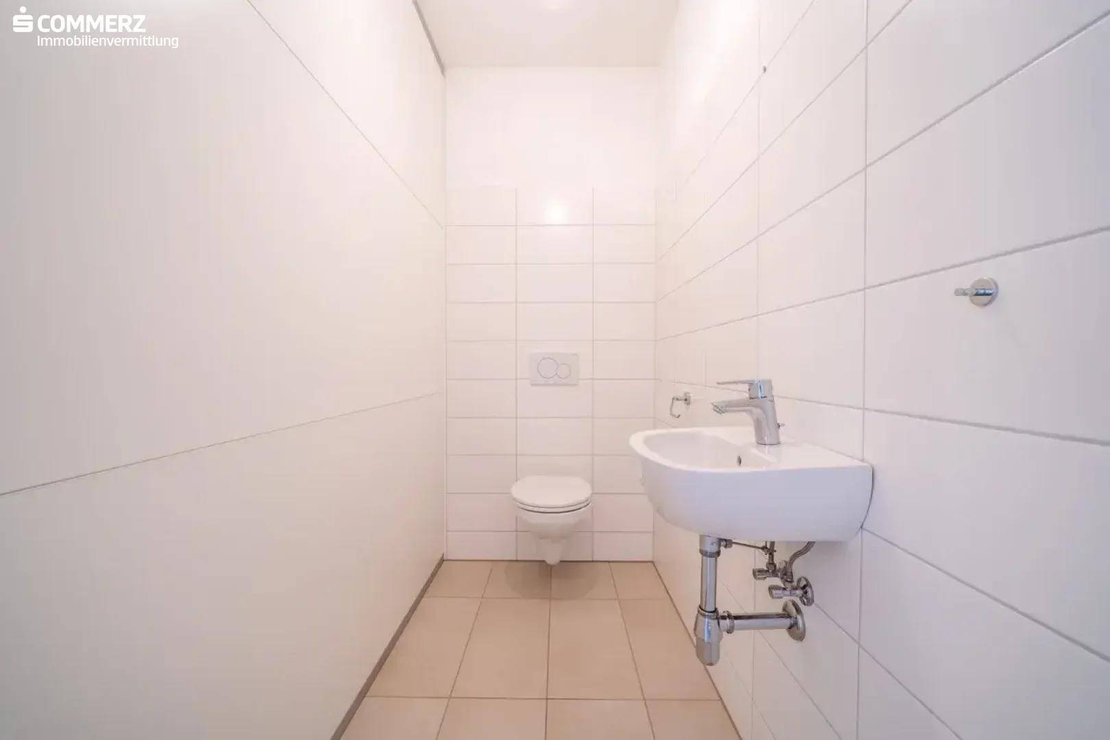 Separates WC mit wandhängender Toilette und kleinem Waschbecken, komplett gefliest.