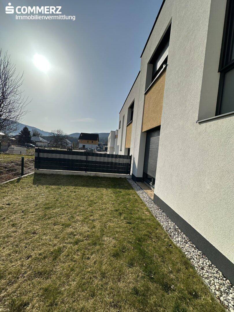 Sonnige Rasenfläche neben einem modernen Reihenhaus mit Blick auf die umliegende Landschaft.