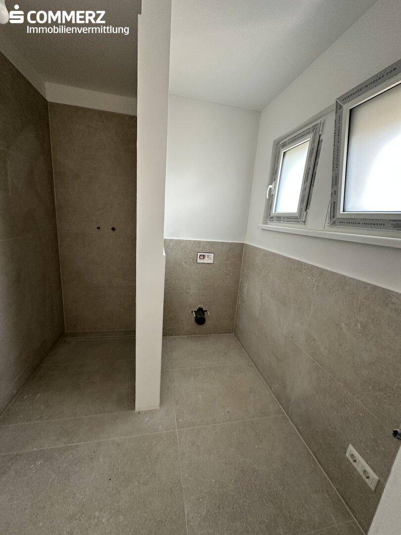 Geräumiges Badezimmer mit modernen Fliesen und Platz für eine Dusche, noch unmöbliert.