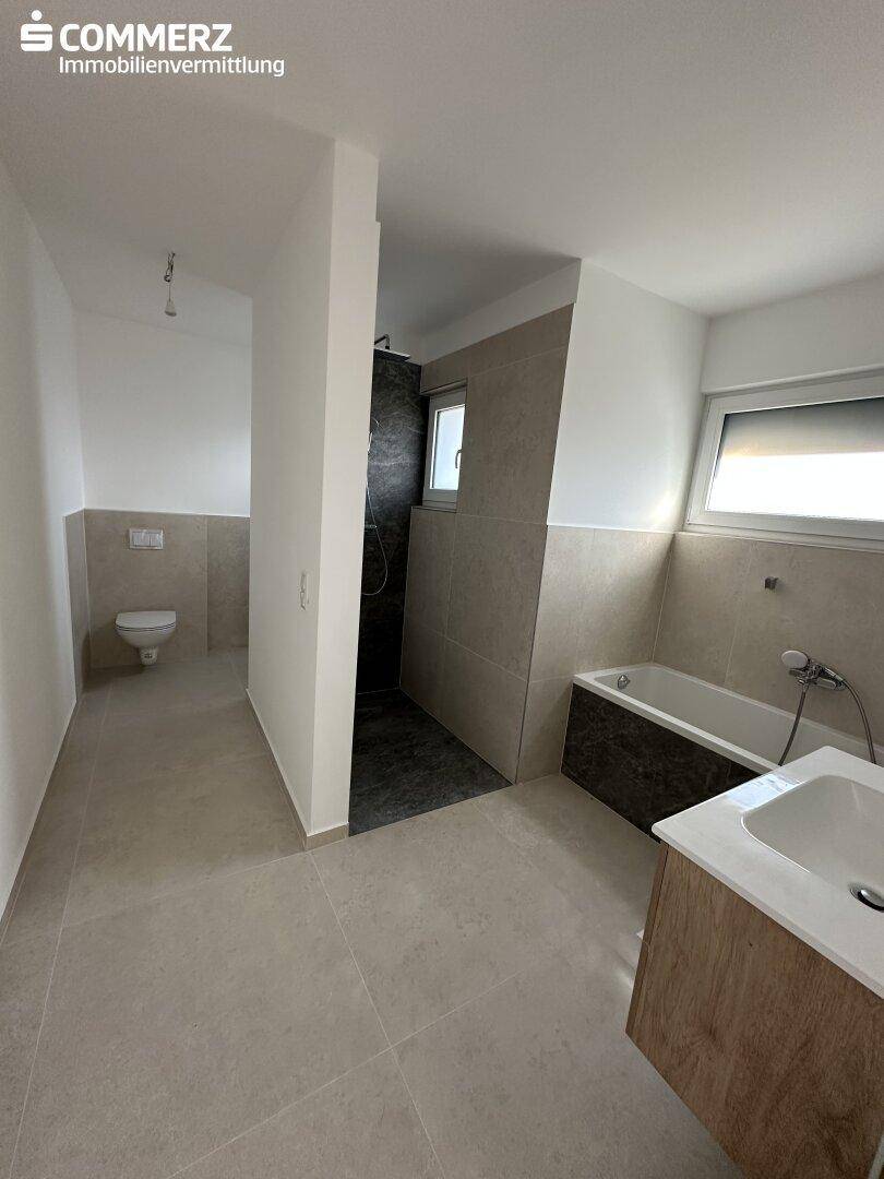 Modernes Badezimmer mit begehbarer Dusche, Badewanne und Wand-WC in neutralen Farbtönen.