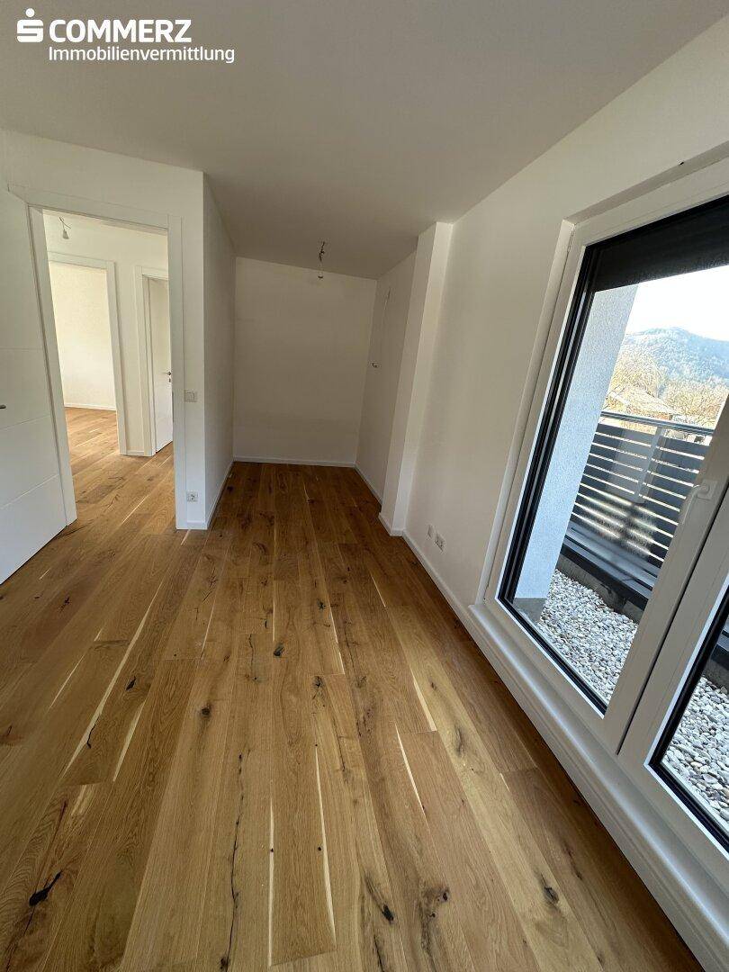 Heller Raum mit Holzboden, großen Fenstern und Zugang zu einem Außenbereich.