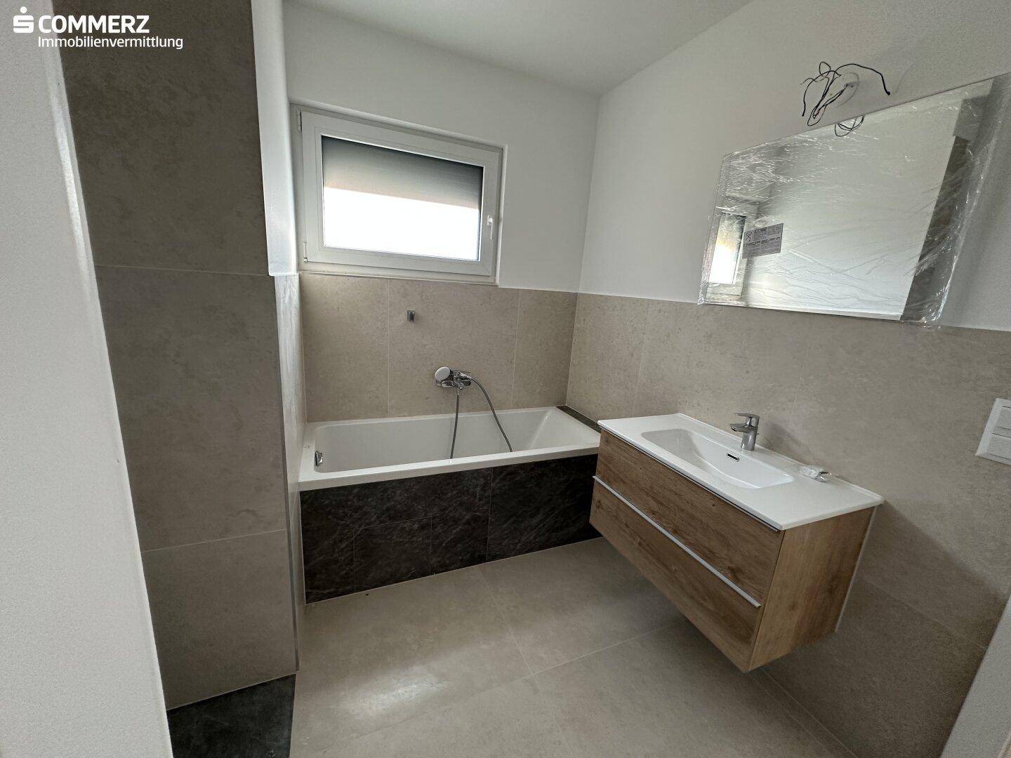 Helles Badezimmer mit Badewanne, modernem Waschtisch und großem Fenster für viel Tageslicht.
