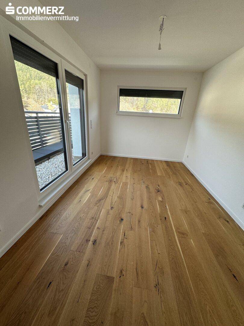 Schlafzimmer mit Holzboden, großen Fenstern und Blick auf die umliegende Natur.