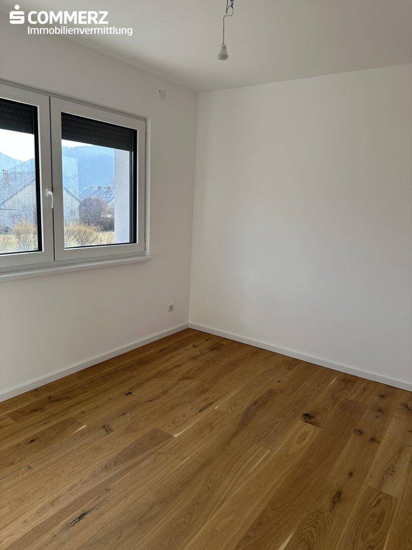 Helles Schlafzimmer mit Holzboden und Fenster, das einen Blick auf die Umgebung bietet.