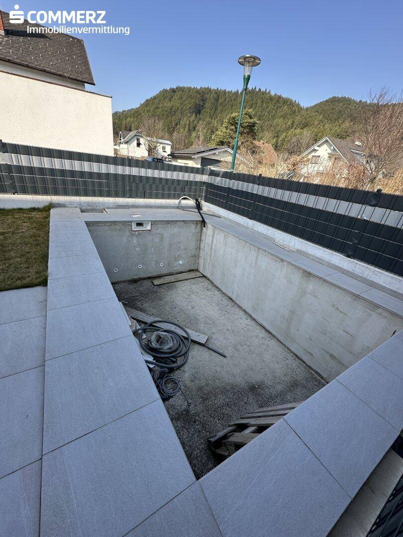 Gartenbereich mit vorbereitetem Poolbecken und gepflasterter Terrasse.