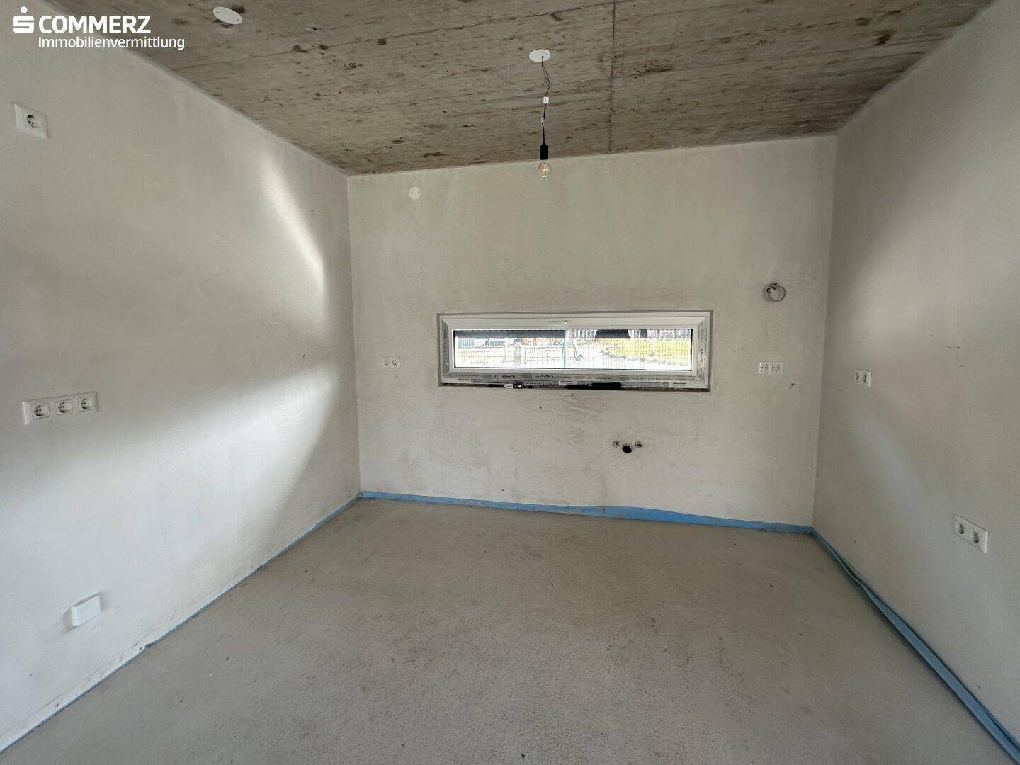 Unfertiger Raum mit kleinem Fenster, Betonboden und sichtbaren Elektroinstallationen.