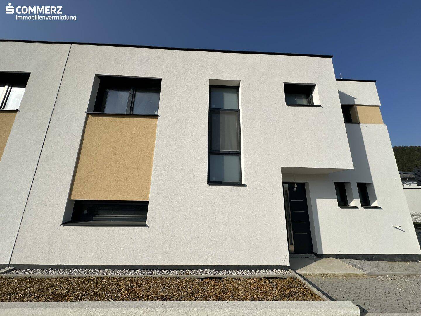 Moderne Architektur eines Reihenhauses mit weißer Fassade und kontrastierenden Fensterrahmen.