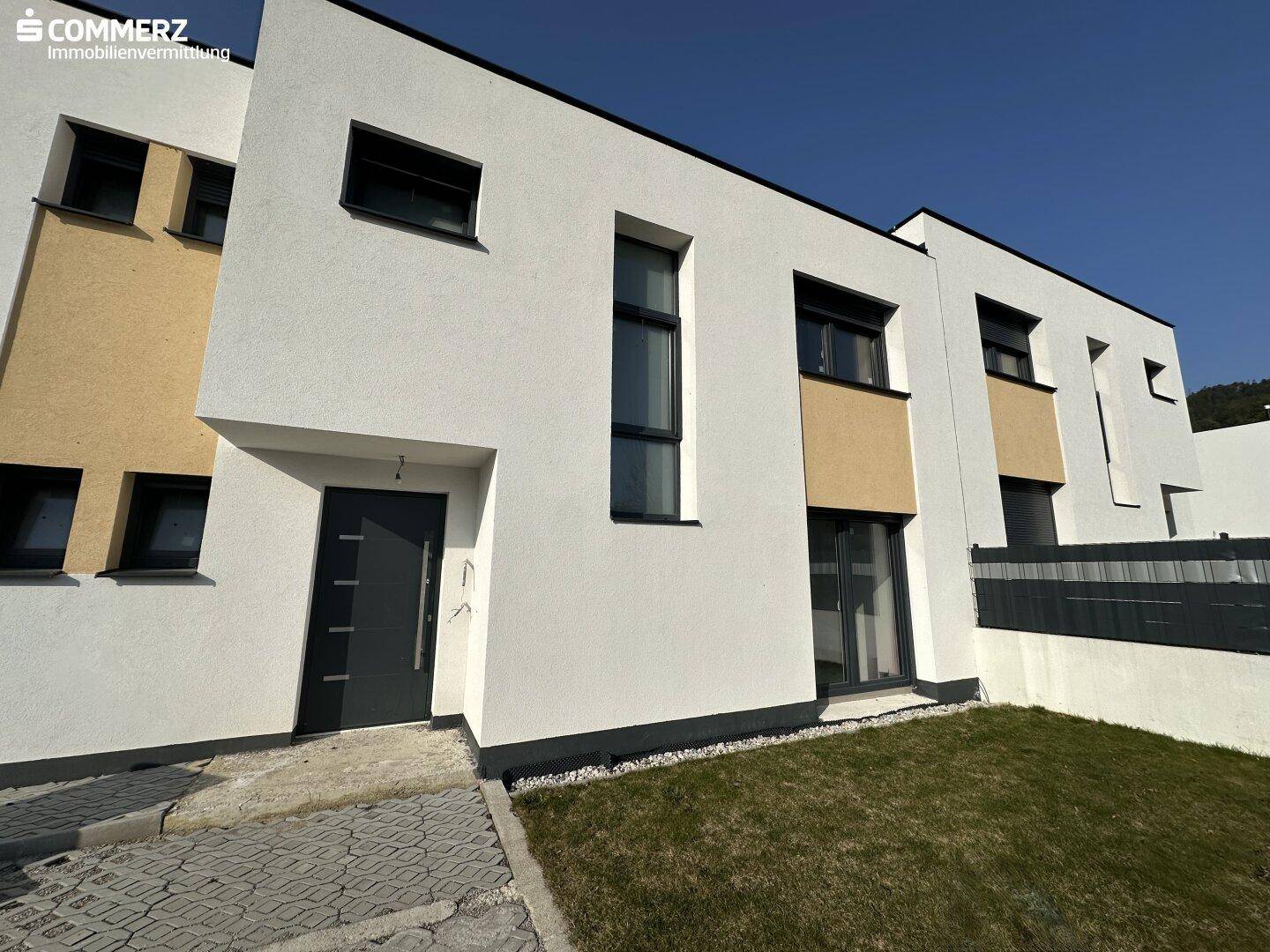 Vorderansicht eines modernen Reihenhauses mit kleinem Vorgarten und gepflastertem Zugang.