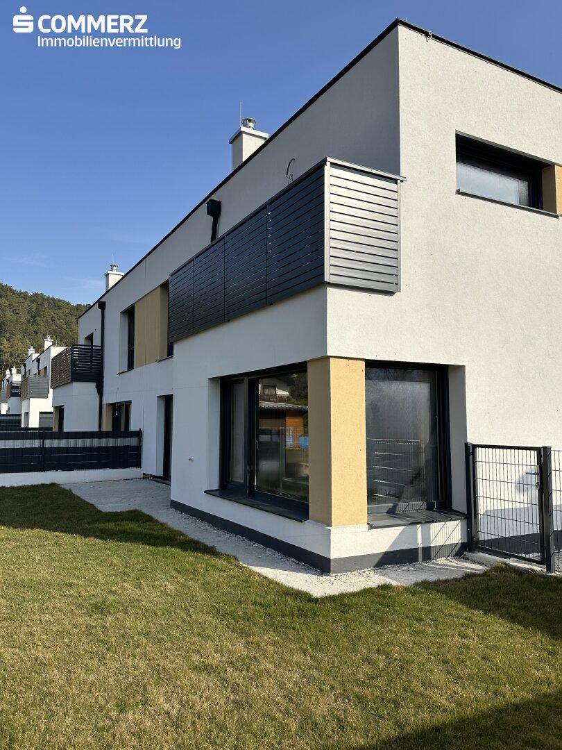 Seitliche Ansicht eines modernen Reihenhauses mit Balkon und gepflegtem Rasenbereich.