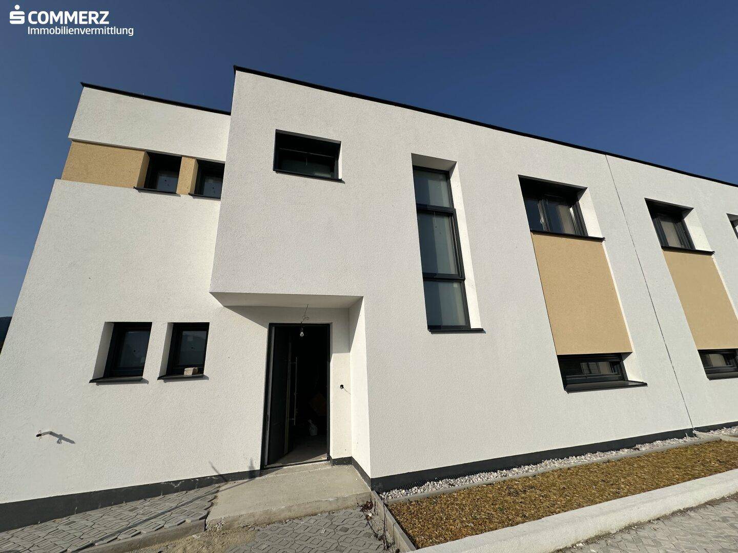 Moderne Hausfassade mit weißem Putz, dunklen Fenstern und Eingangsbereich.