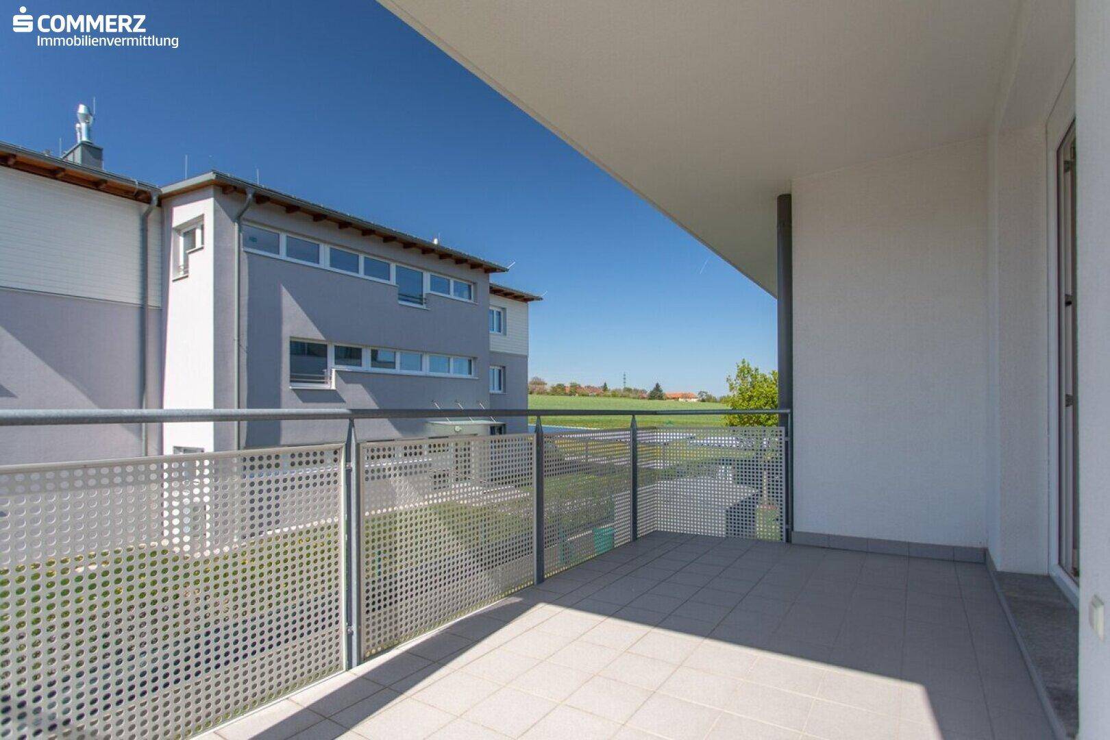 Balkon mit Fliesenboden und Blick auf das Nachbargebäude sowie eine grüne Wiese.