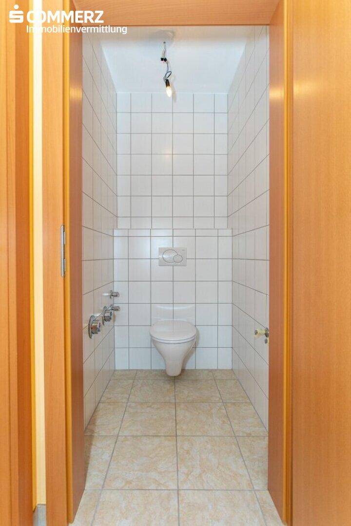 Separates WC mit Wand-WC und weißen Fliesen, praktisch und funktional gestaltet.
