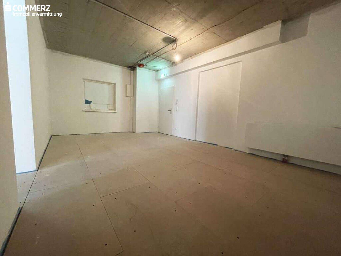 Leerer Raum im Rohbau mit temporärem Bodenbelag und einer Nische in der Wand, bereit für die Fertigstellung.