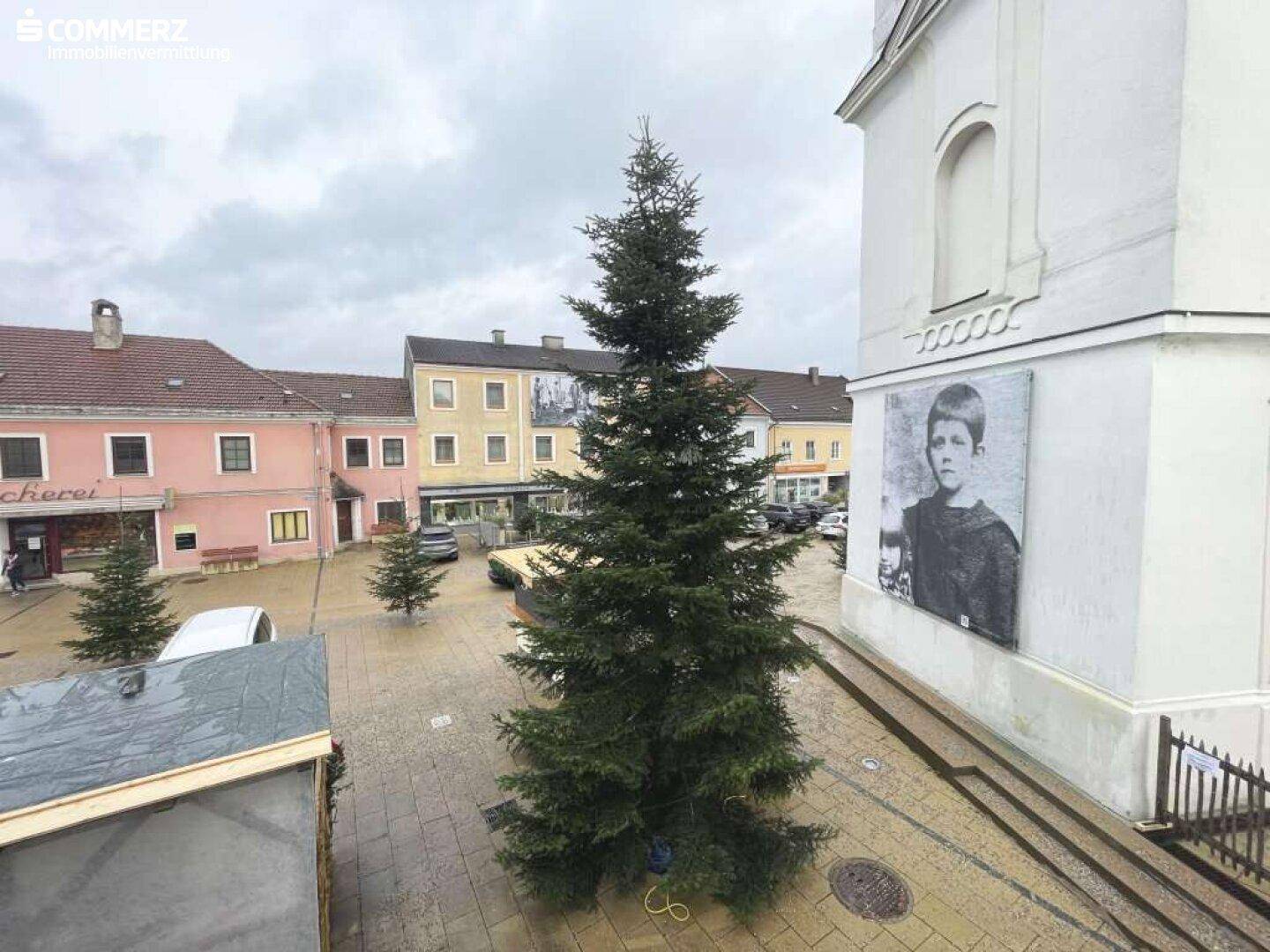 Blick auf einen belebten Stadtplatz mit einem großen Weihnachtsbaum und historischen Gebäuden unter bewölktem Himmel.