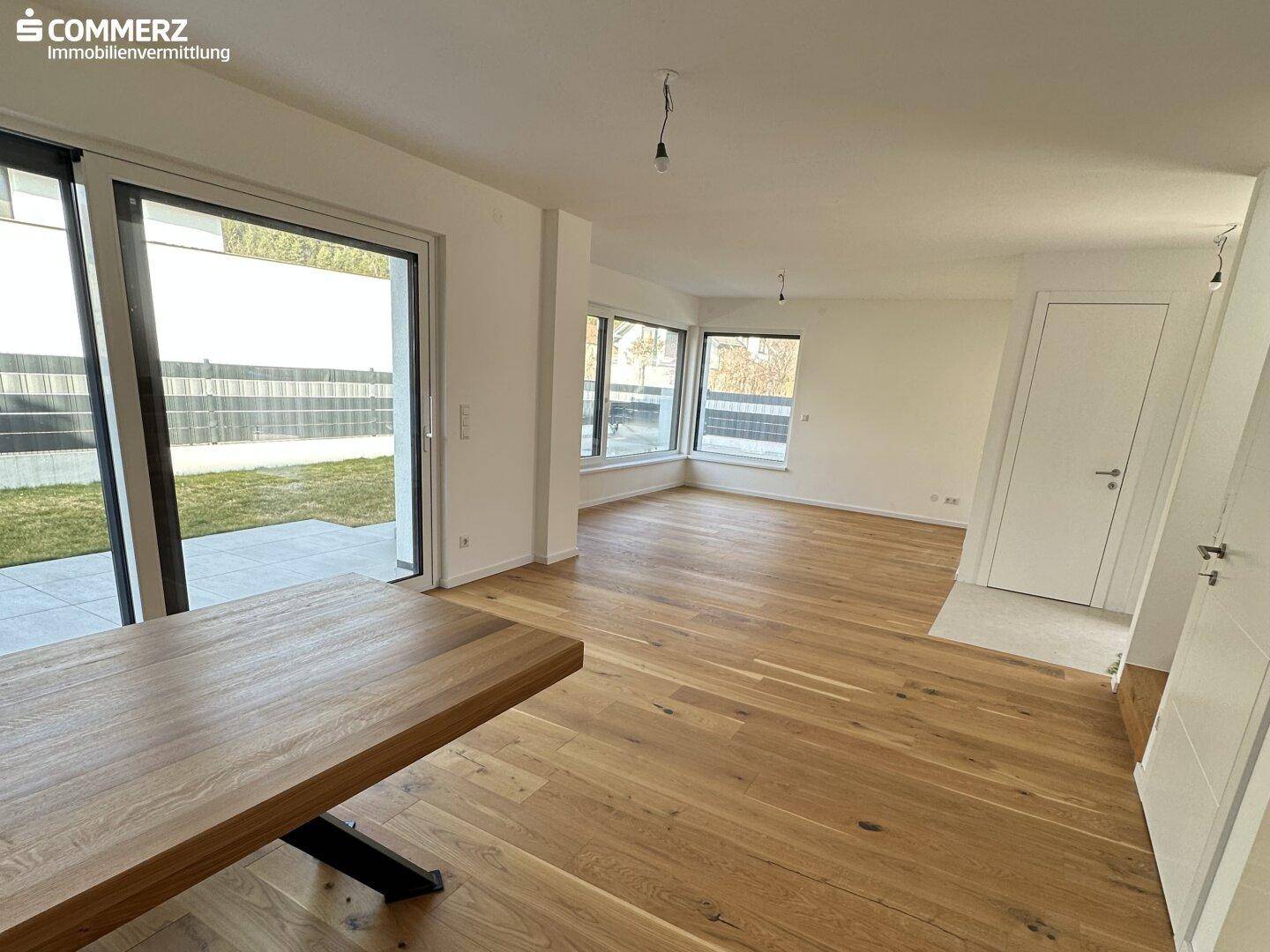 Geräumiger Wohnbereich mit Holzboden, großen Fenstern und direktem Zugang zum Garten.