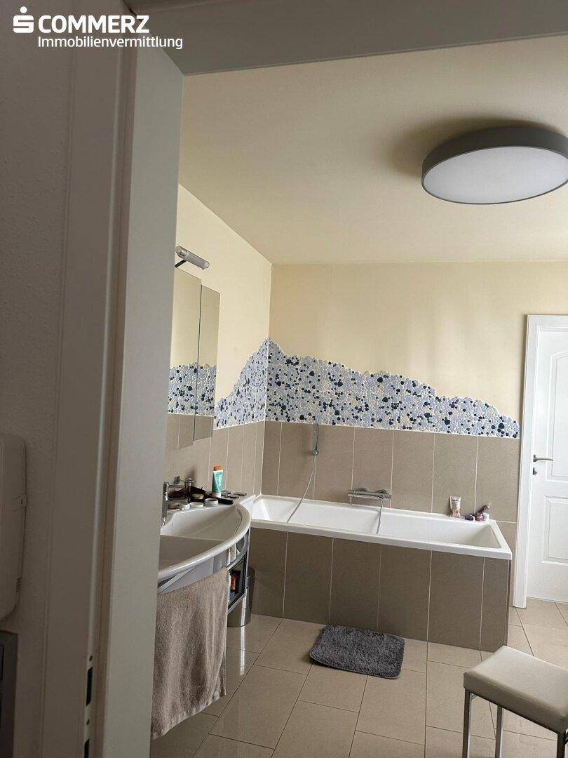 Badezimmer mit Badewanne, gefliesten Wänden und einem modernen Doppelwaschbecken.