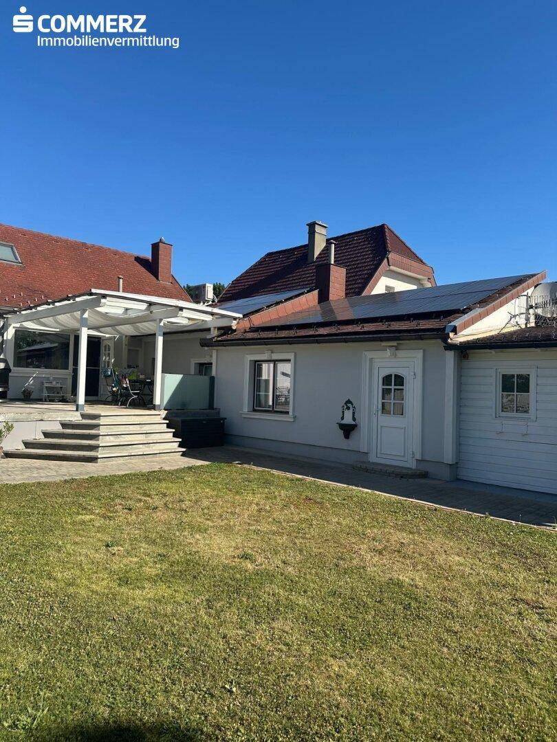 Rückansicht des Hauses mit großer Terrasse, Garten und Photovoltaikanlage auf dem Dach.