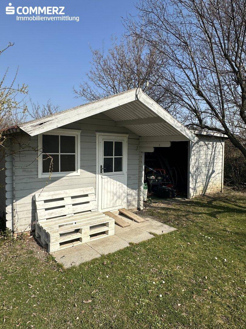 Rustikales Gartenhaus aus Holz mit kleiner Veranda und Stauraum für Gartengeräte.