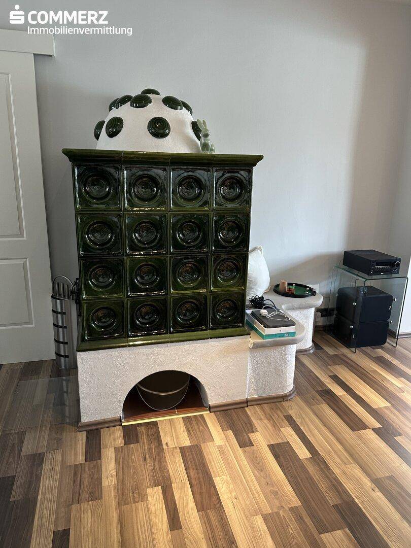 Wohnzimmer mit grünem Kachelofen als zentrales Heizelement und Laminatboden.