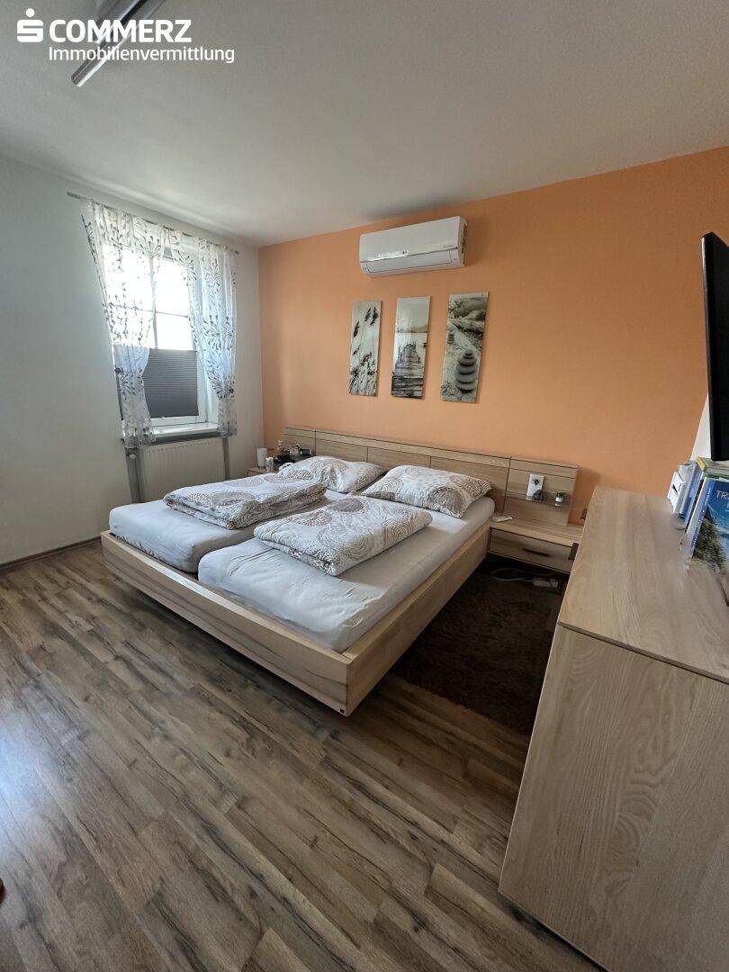 Schlafzimmer mit Doppelbett, Laminatboden und Klimaanlage an der Wand.
