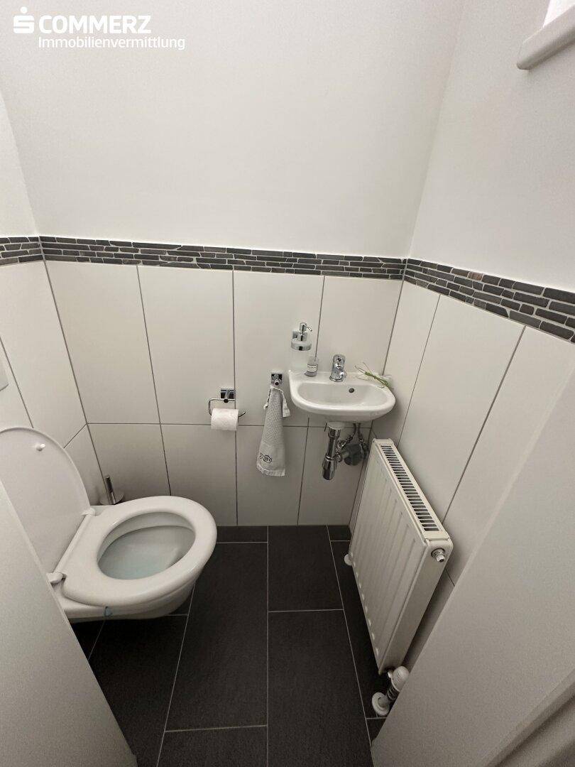 Kleines Gäste-WC mit Wand-WC, Handwaschbecken und dunklen Bodenfliesen.