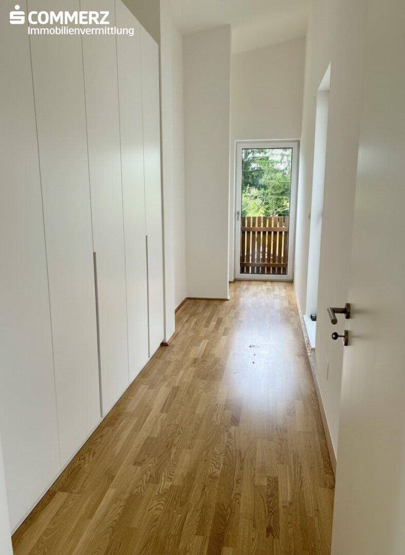 Heller Flur mit Einbauschränken, Parkettboden und Zugang zu einem Balkon.