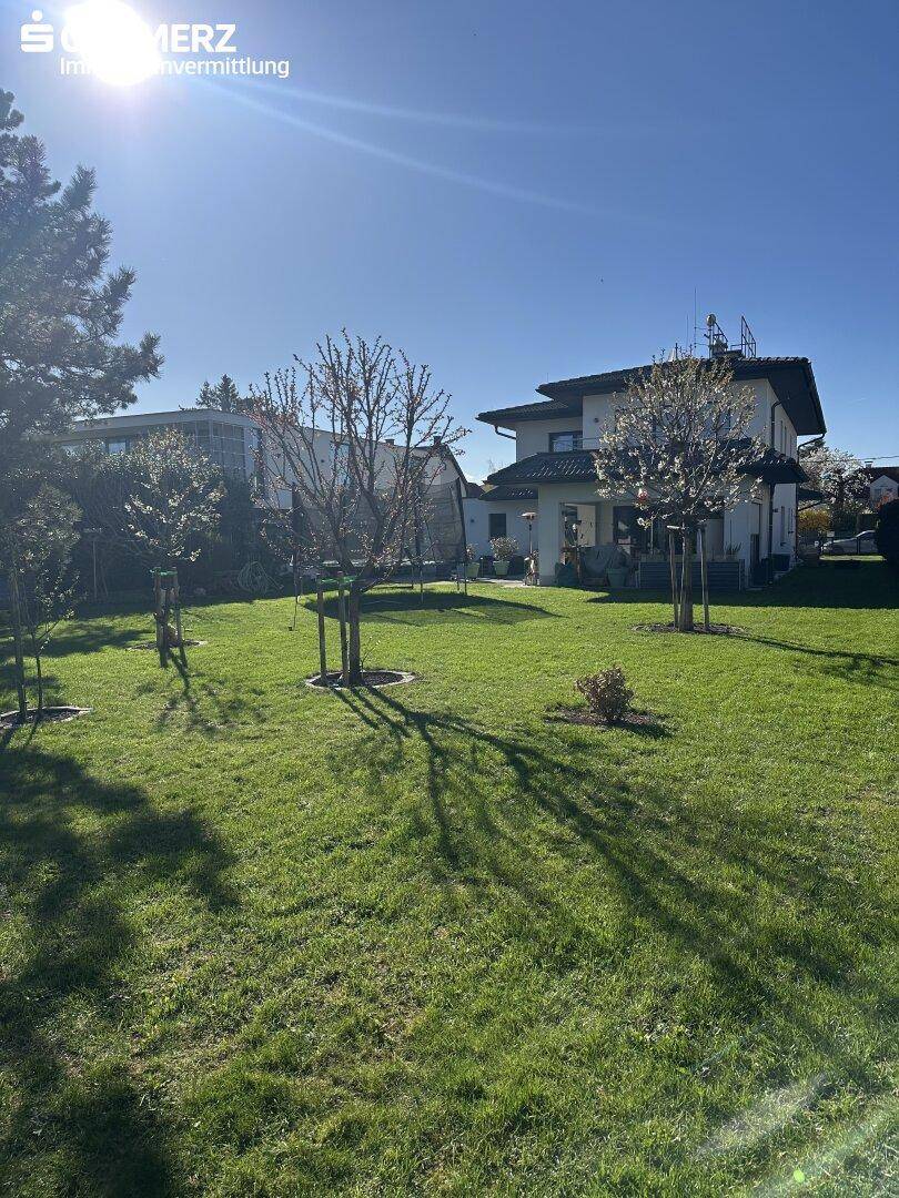 Sonniger Garten mit weitläufiger Rasenfläche und Blick auf das moderne Wohnhaus.
