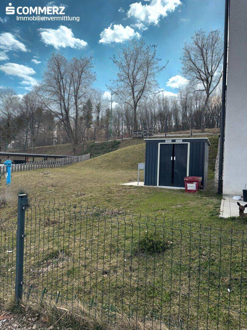 Grüner Gartenbereich mit Rasenfläche und einem praktischen Gartenschuppen am Hang.