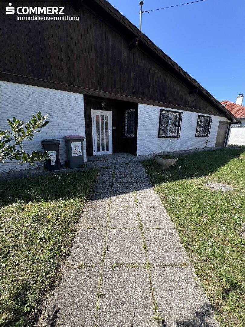 Eingangsbereich des Hauses mit einem gepflasterten Weg und weißer Ziegelfassade.