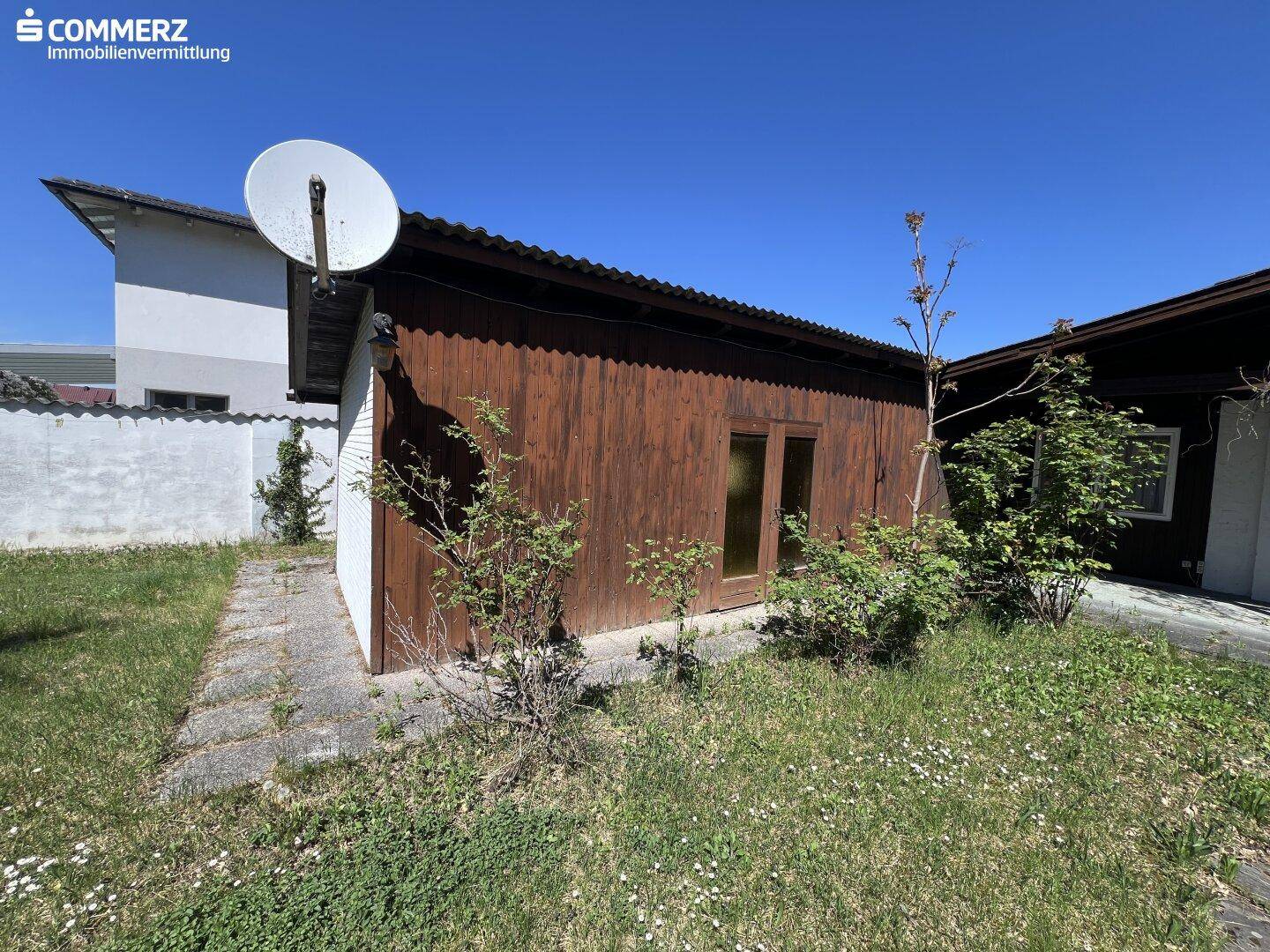 Hölzerner Gartenschuppen mit Satellitenschüssel und umgebender Rasenfläche im Garten.