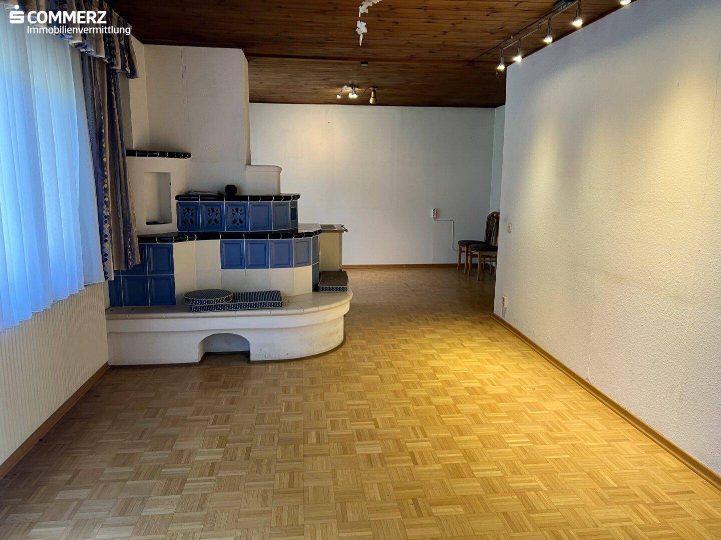 Geräumiges Wohnzimmer mit Parkettboden, Holzbalkendecke und einem traditionellen Kachelofen.
