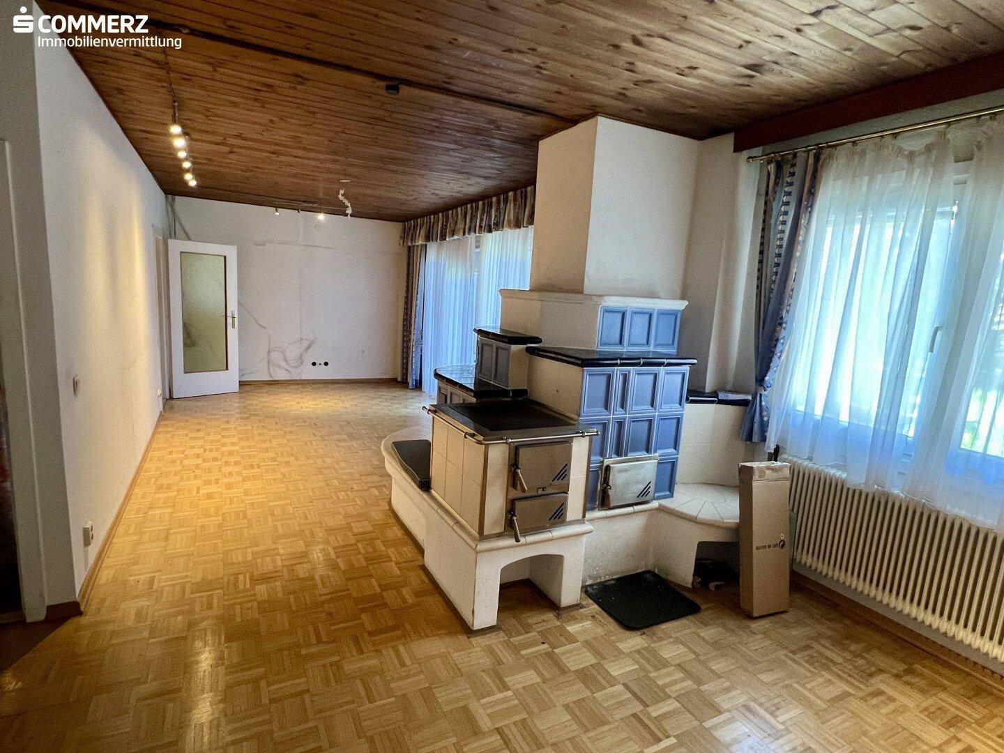 Helles Wohnzimmer mit Kachelofen, Parkettboden und Fenstern mit Blick ins Grüne.
