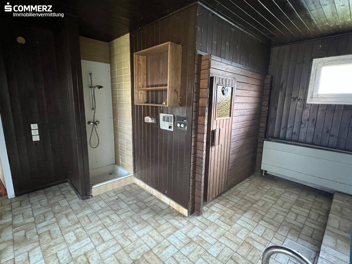 Wellnessbereich mit Sauna, Dusche und gefliestem Boden in Holzoptik.