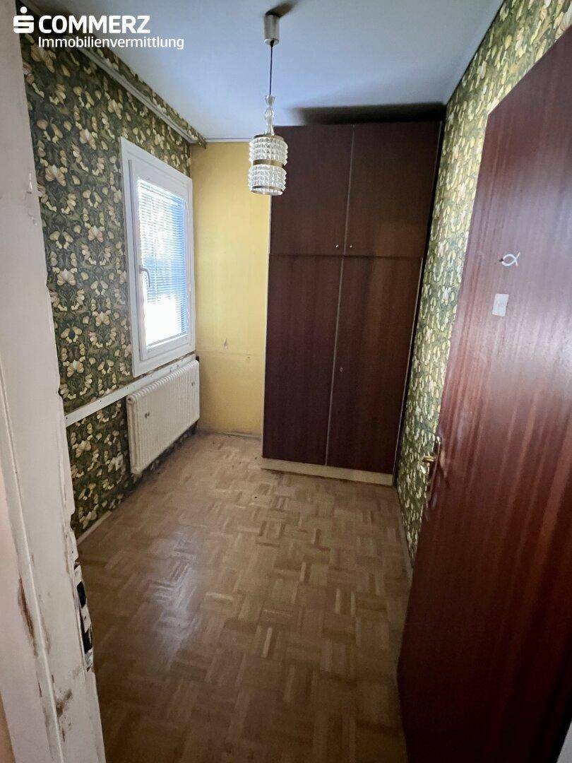 Kleines Schlafzimmer mit Parkettboden, floraler Tapete und einem Einbauschrank.