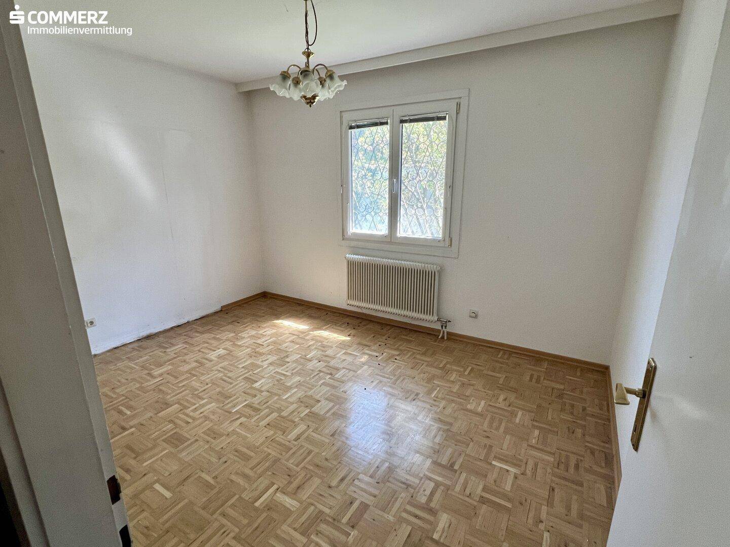 Helles Schlafzimmer mit Parkettboden, weißen Wänden und einem großen Fenster.