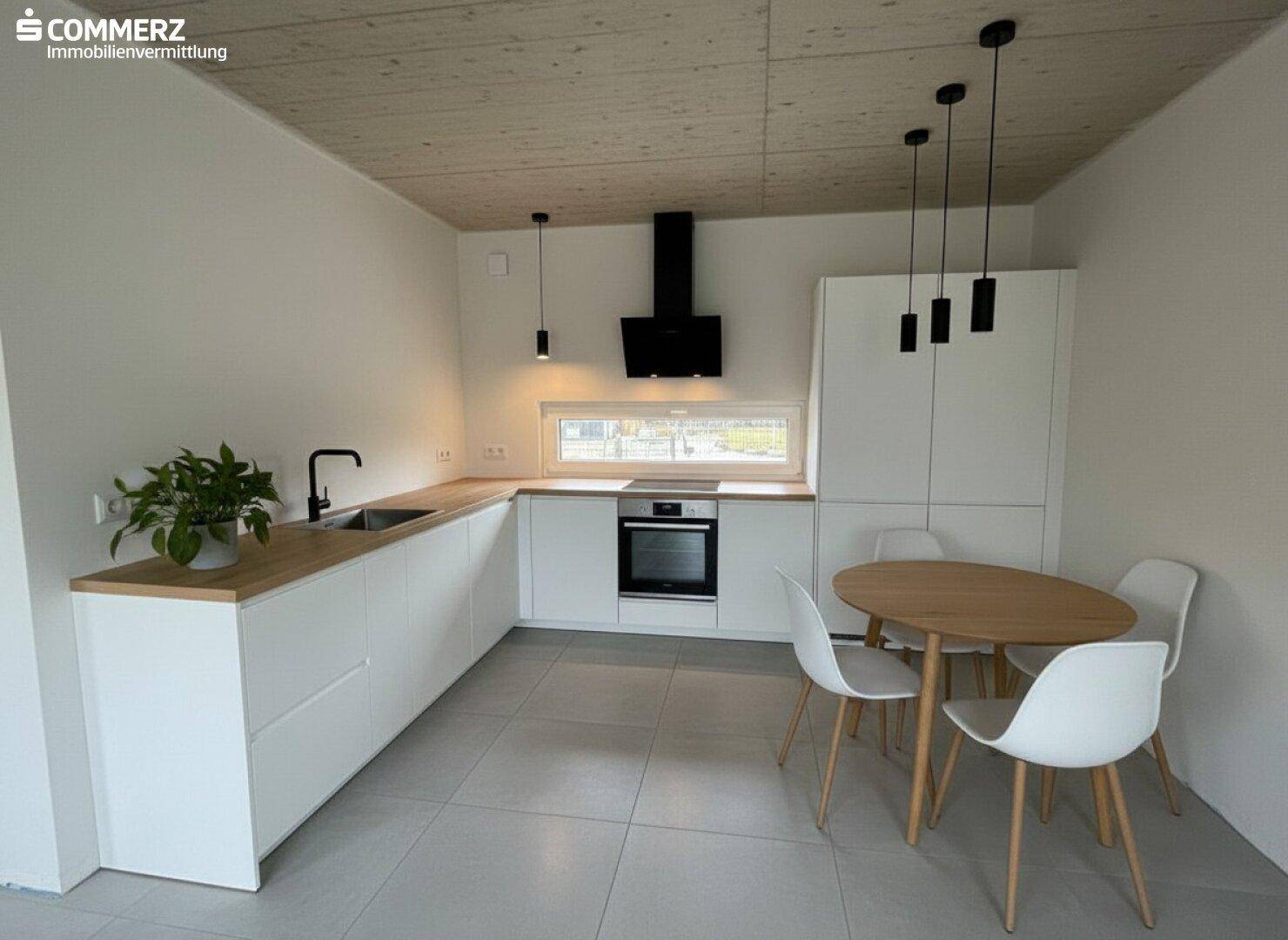 Moderne Küche mit weißen Schränken, Holzarbeitsplatte und Essbereich unter Holzbalkendecke.