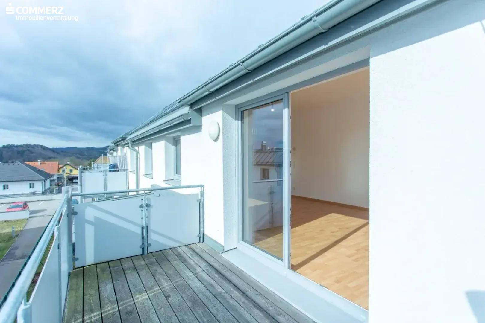 Geräumiger Balkon mit Holzboden und Glasgeländer, bietet weite Aussicht auf die Umgebung.