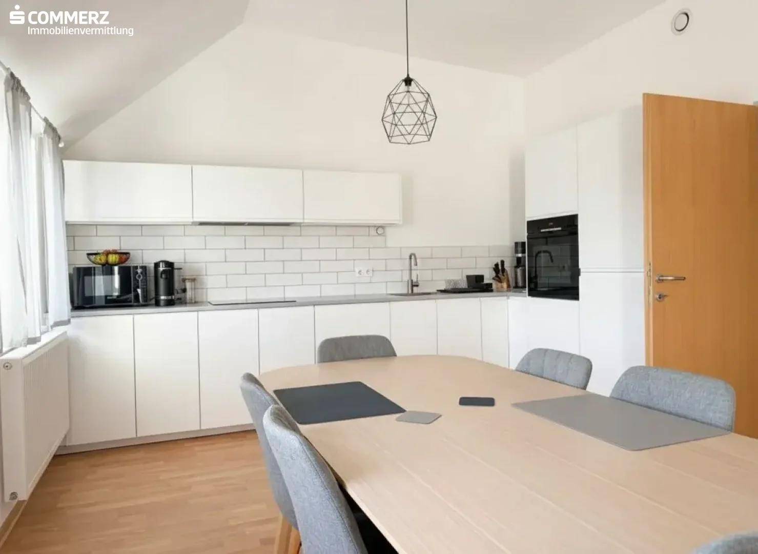 Moderne Küche mit weißen Schränken, Essbereich und Dachschräge, ideal für geselliges Kochen.