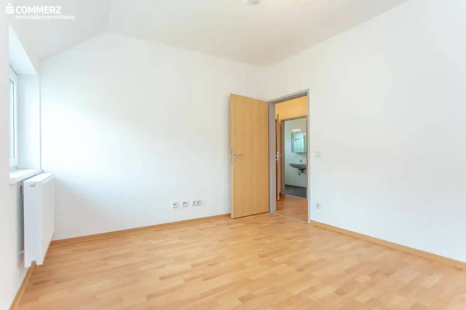 Schlafzimmer mit Holzboden und Zugang zu einem angrenzenden Badezimmer, hell und geräumig.