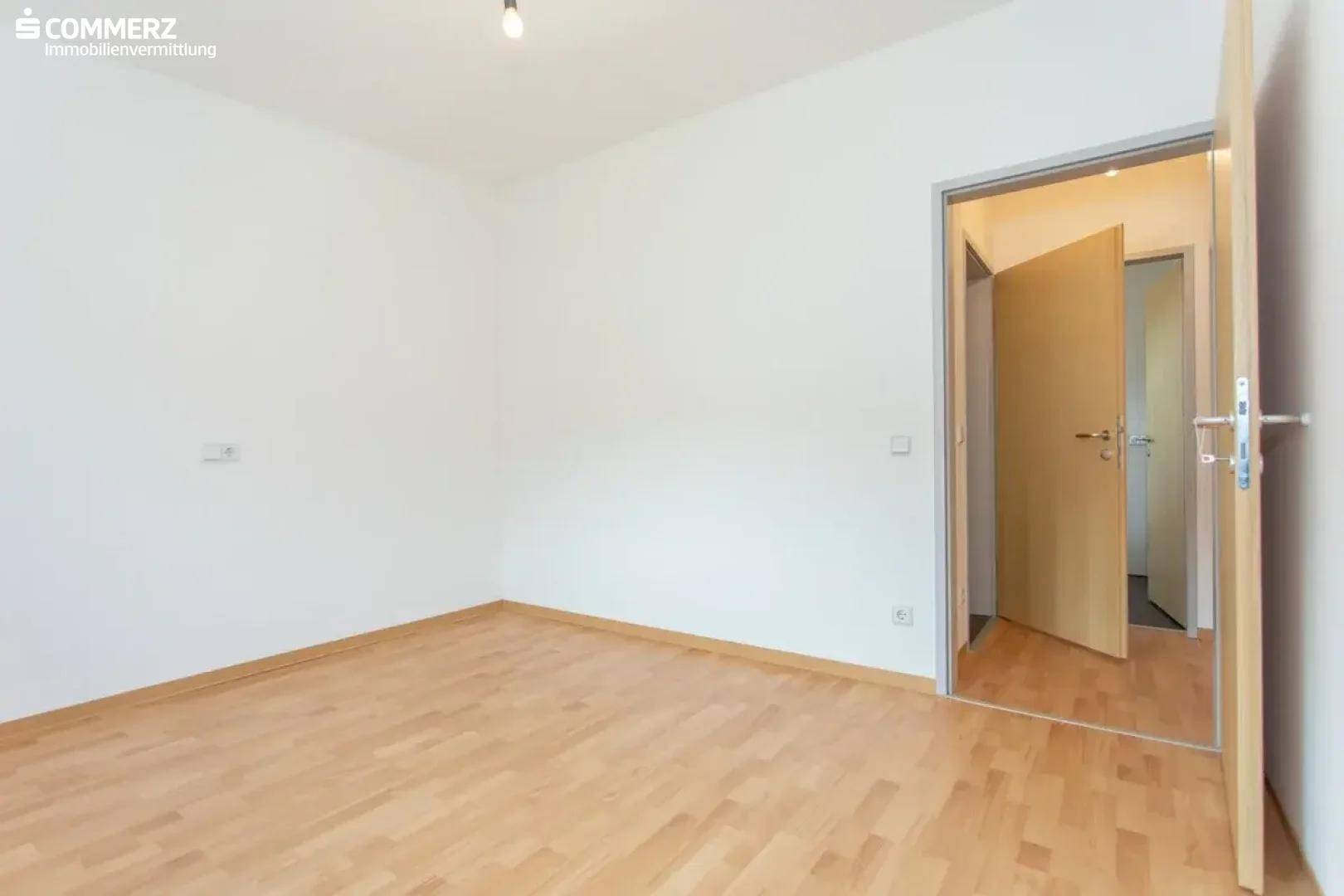 Helles Schlafzimmer mit Holzboden und weiß gestrichenen Wänden, bietet Zugang zu weiteren Räumen.