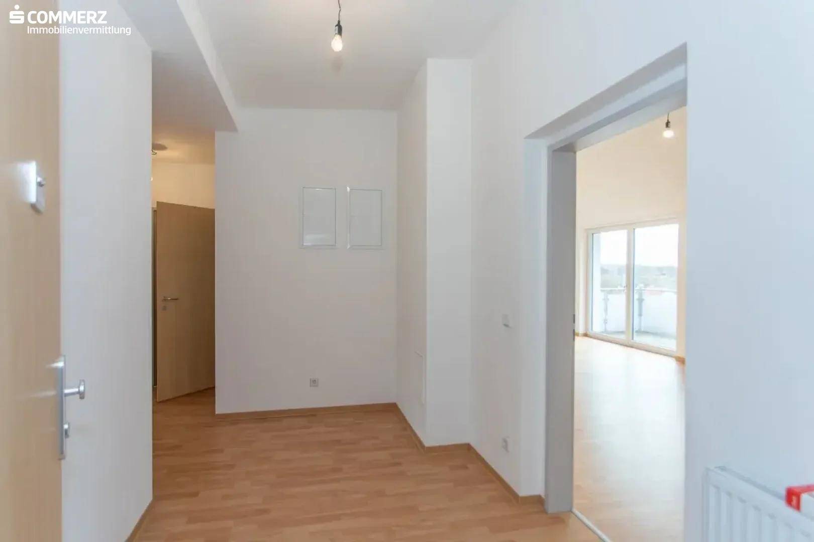 Heller Eingangsbereich mit Holzboden, der in einen offenen Wohnbereich führt.