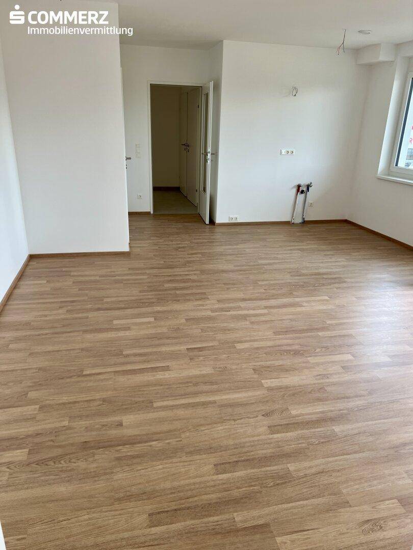 Geräumiger, leerer Wohnbereich mit hellem Laminatboden und Zugang zu weiteren Räumen.
