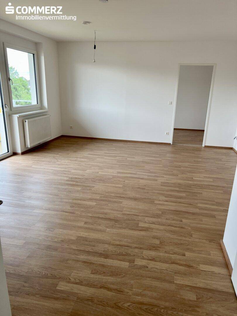 Heller Wohnbereich mit Laminatboden und großem Fenster mit Zugang zum Balkon.