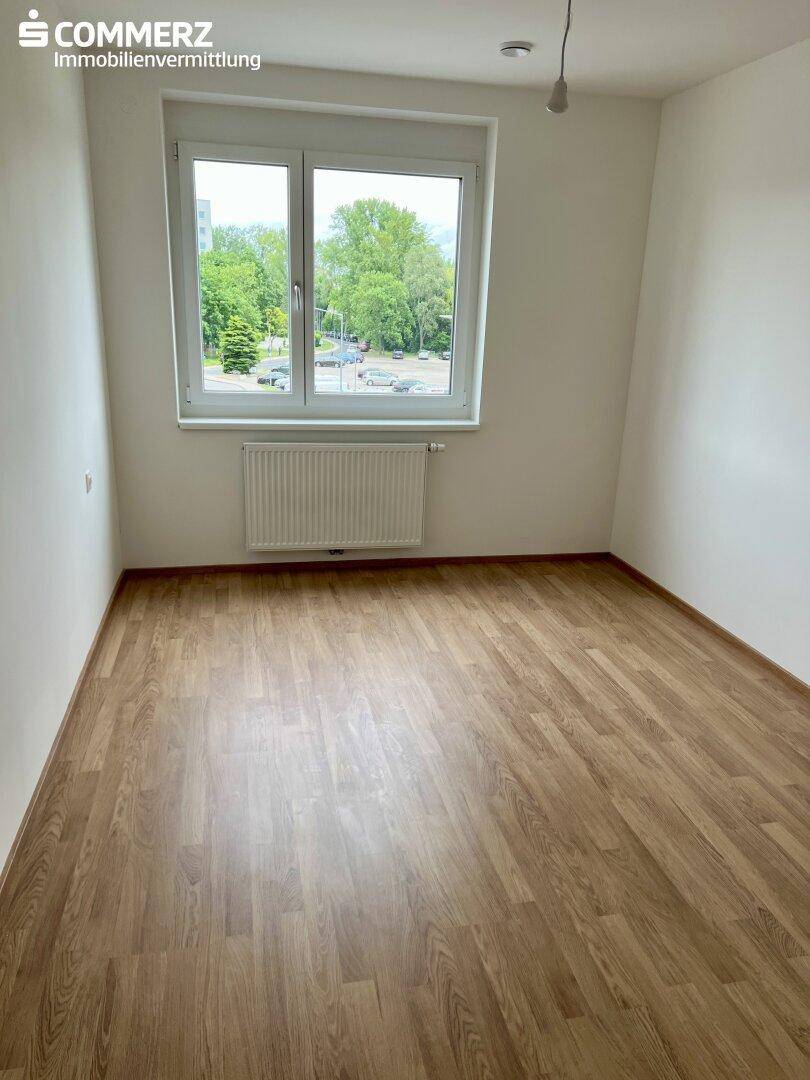 Unmöbliertes Schlafzimmer mit Laminatboden und einem großen Fenster, das viel Licht spendet.