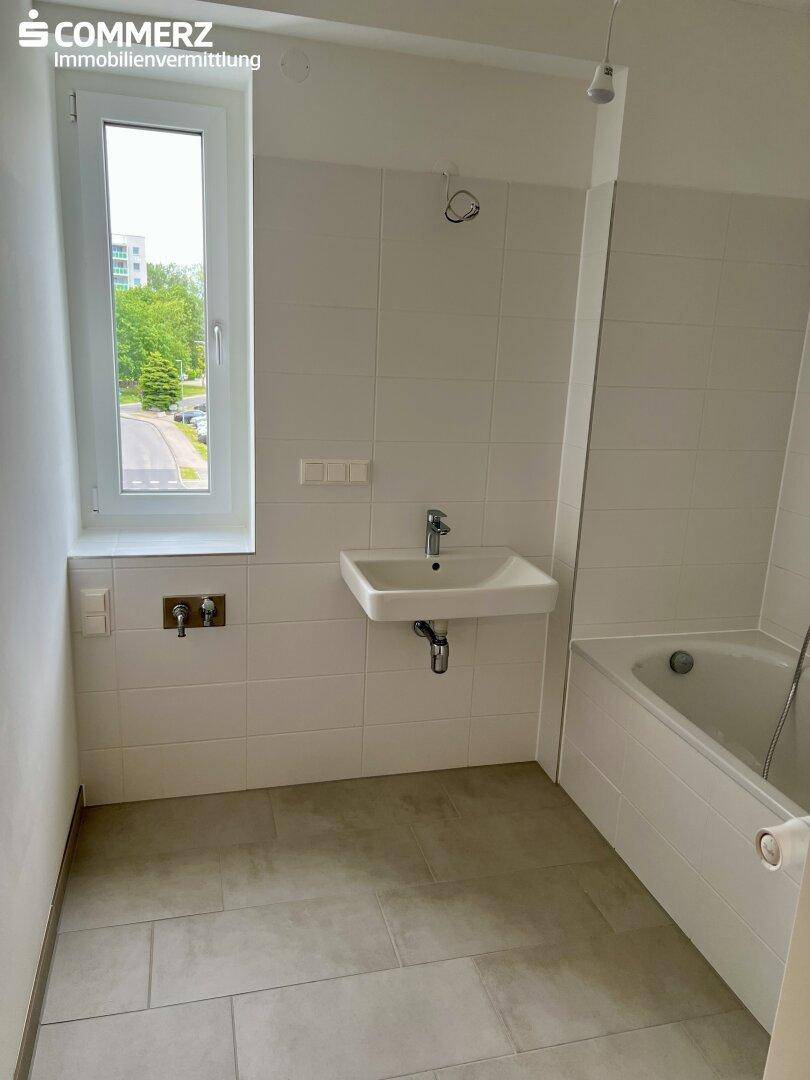Unmöbliertes Badezimmer mit Badewanne, Waschbecken und einem Fenster für natürliche Belüftung.