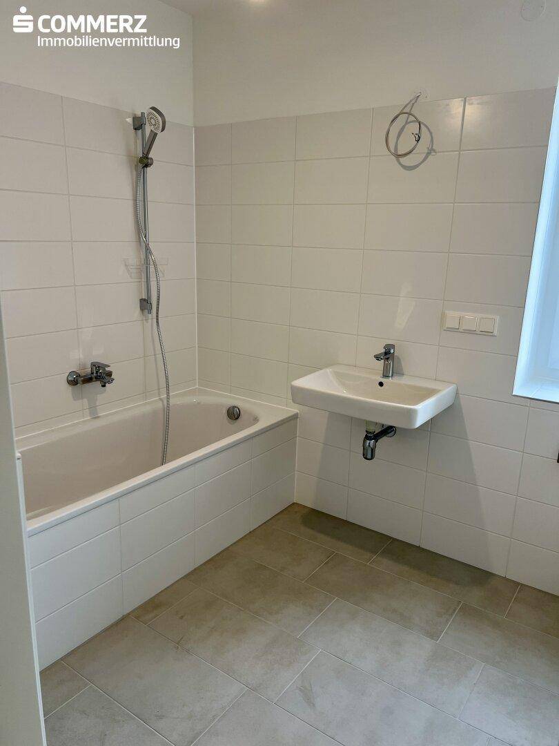 Badezimmer mit Badewanne, Dusche, Waschbecken und Fenster.