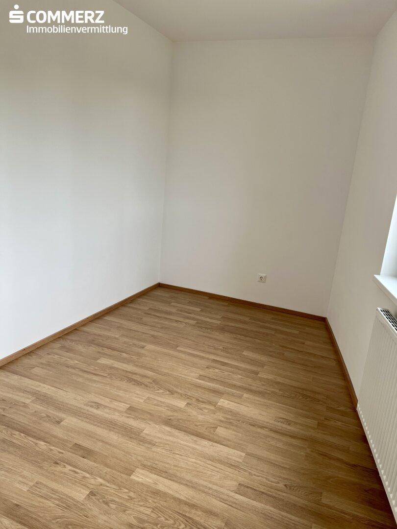 Leeres Zimmer mit Laminatboden und Fenster, ideal als Schlaf- oder Arbeitszimmer.