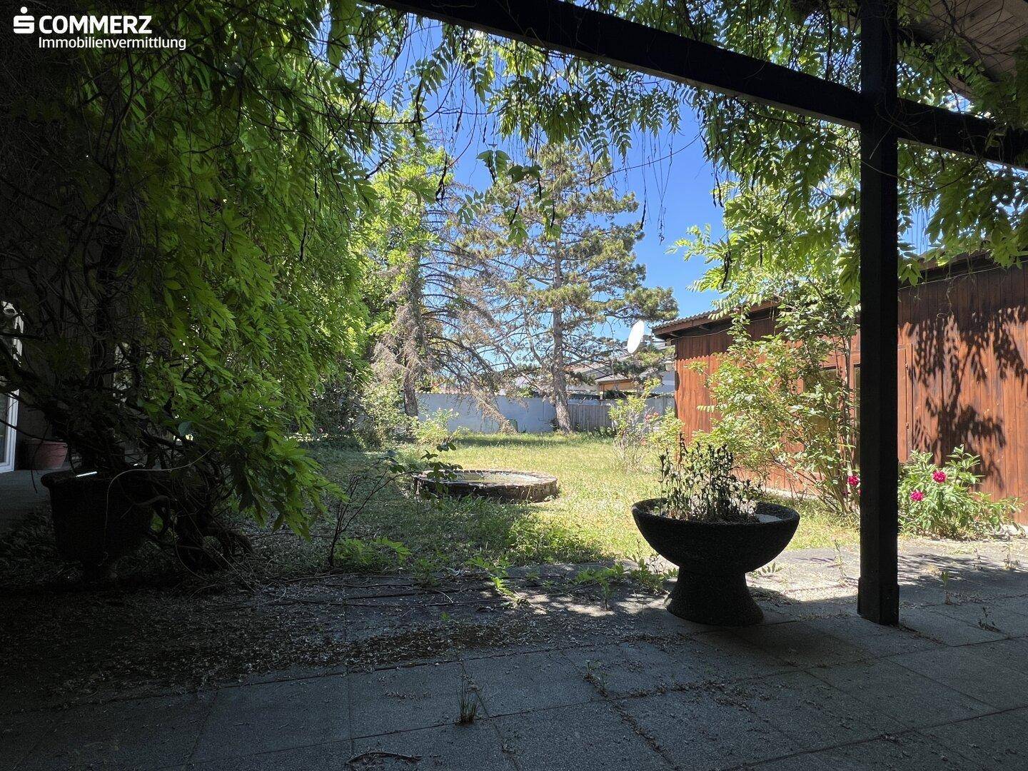 Geräumige Terrasse mit Pergola und Blick auf den sonnigen Gartenbereich mit Bäumen.