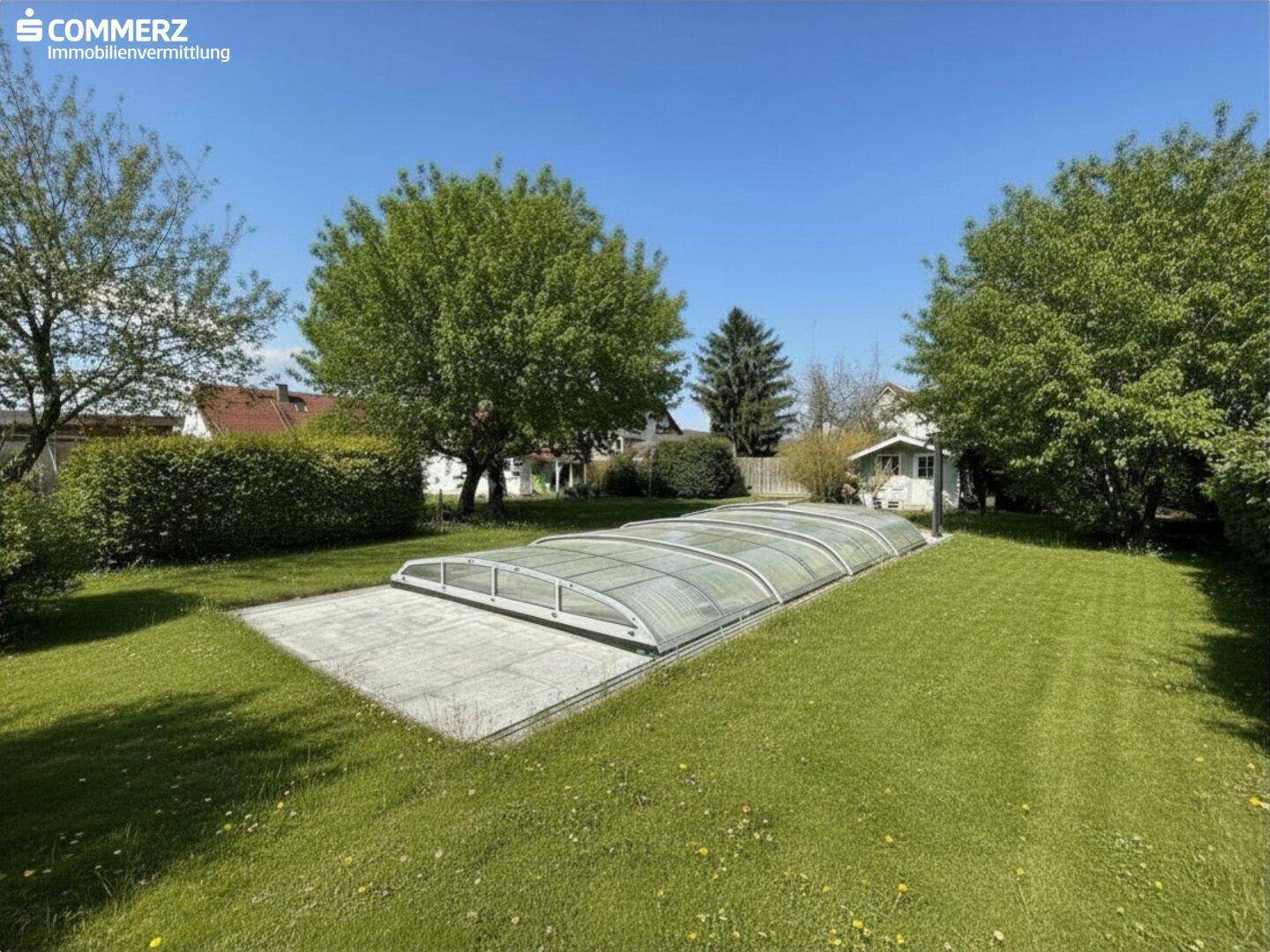 Gepflegter Garten mit überdachtem Swimmingpool, Rasenfläche und altem Baumbestand.